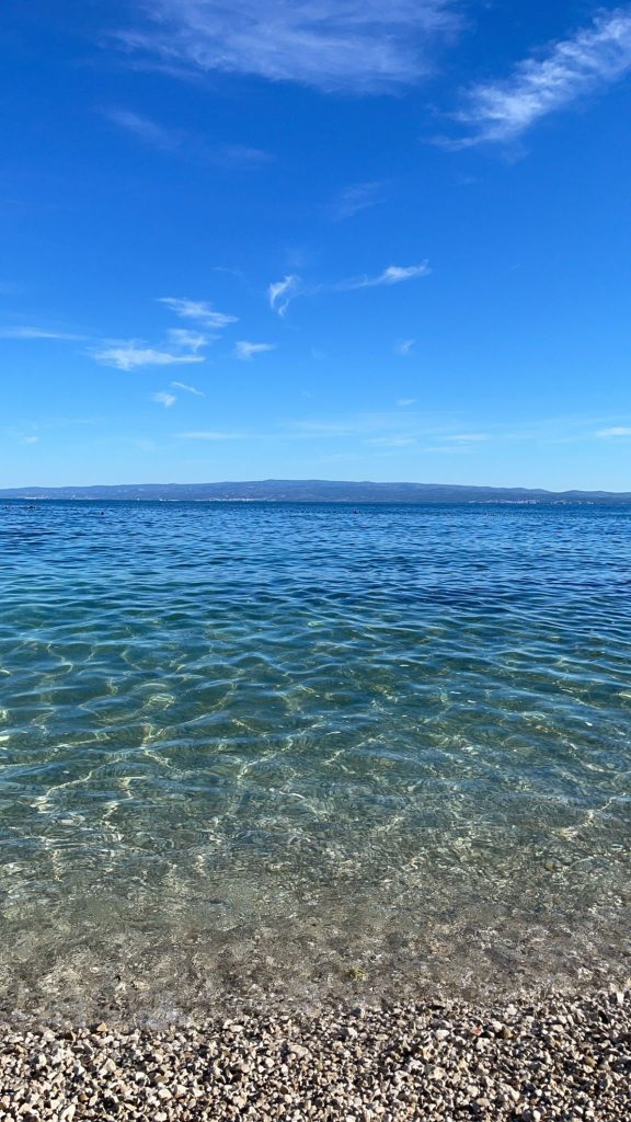 Bright, blue sky and crystal clear ocean from the shore. The shore line is rocky.