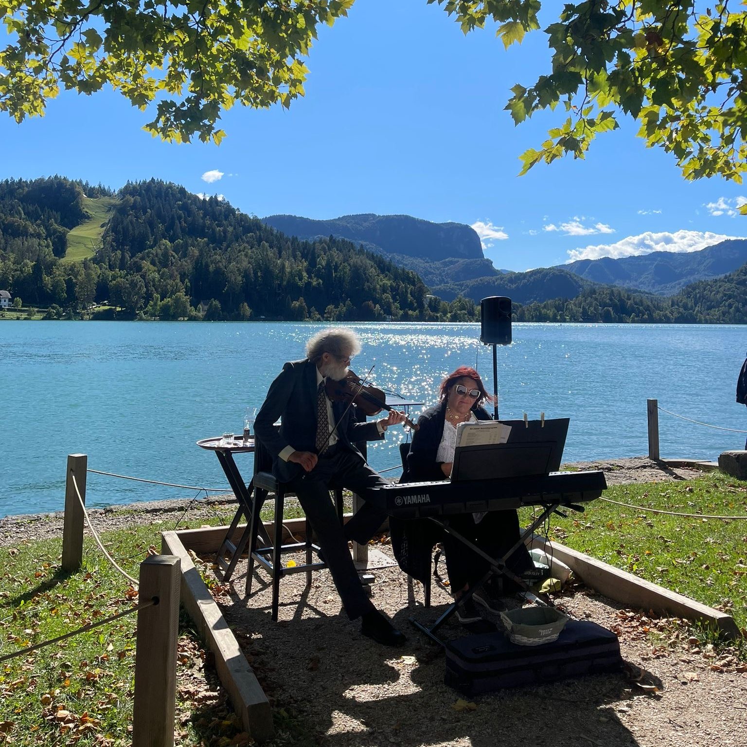 Man playing violin and woman playing piano next to Lake Como. 