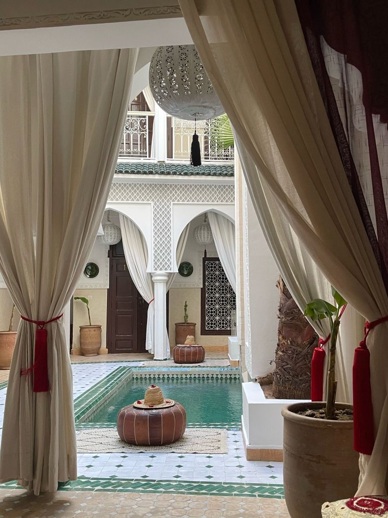 Riad courtyard with pool, curtain-framed view, and arched windows in the background